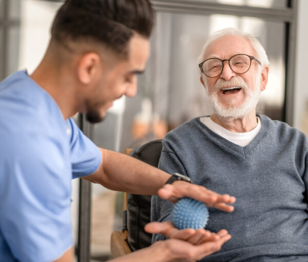 Joyous aged man undergoing a session of physical therapy conducted by an experienced rehabilitation doctor